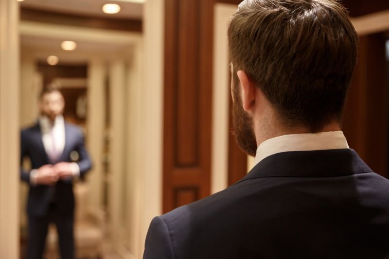 man getting dressed in to a suit in front of a mirror