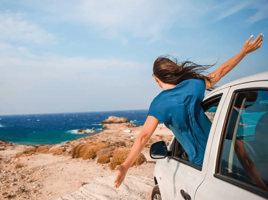 Woman with her head out the window of a car at the beach