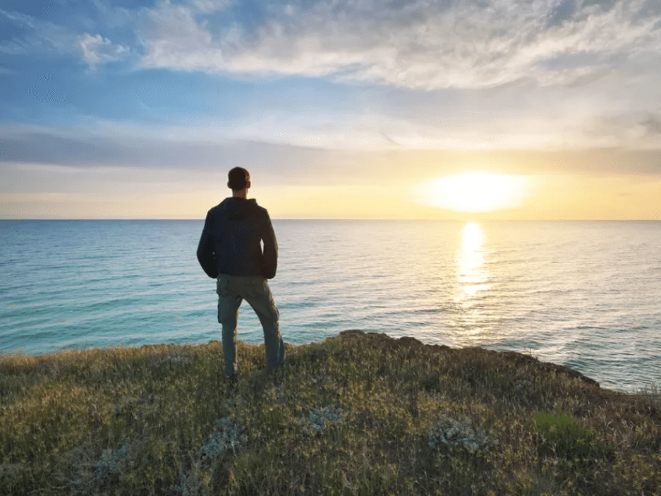 Man standing in front of the ocean at sunset