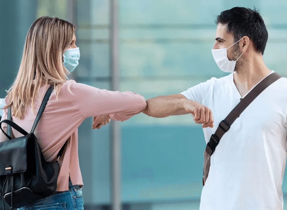 Two people wearing masks and bumping elbows
