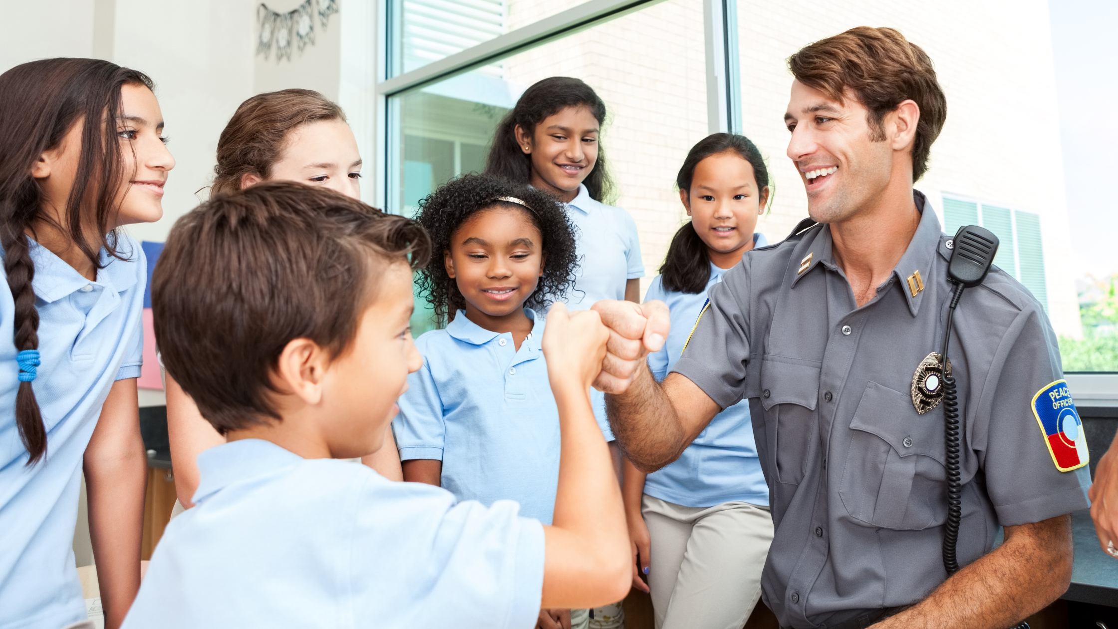 "Smiling police officer fist-bumping an elementary school student during a classroom drug prevention lesson, surrounded by diverse children in school uniforms"