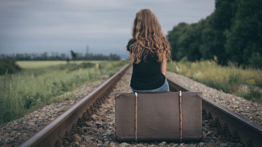 Young girl sitting on a suitcase on a train track